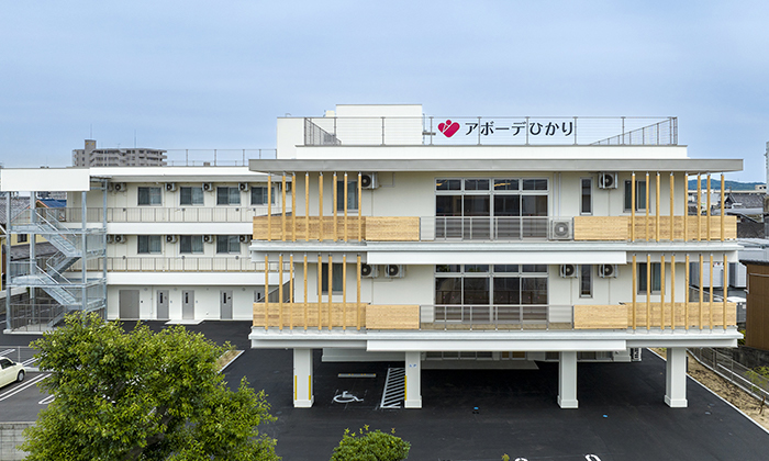 介護施設アボーデひかりの建物外観。白と黄色を基調とした3階建ての施設
