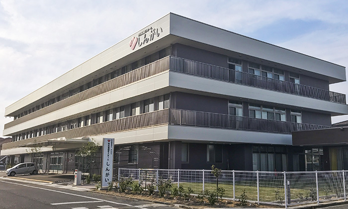 介護施設の建物外観。複数階建てで全面バルコニー付きの新しい施設。
